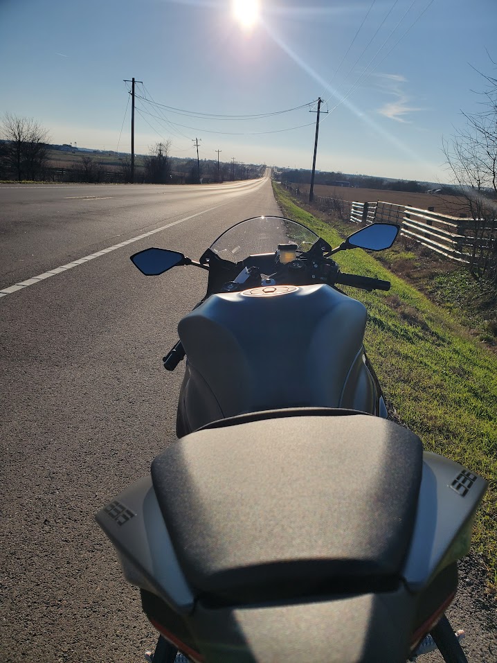 View over a parked Kawasaki Ninja toward a sunlit open road